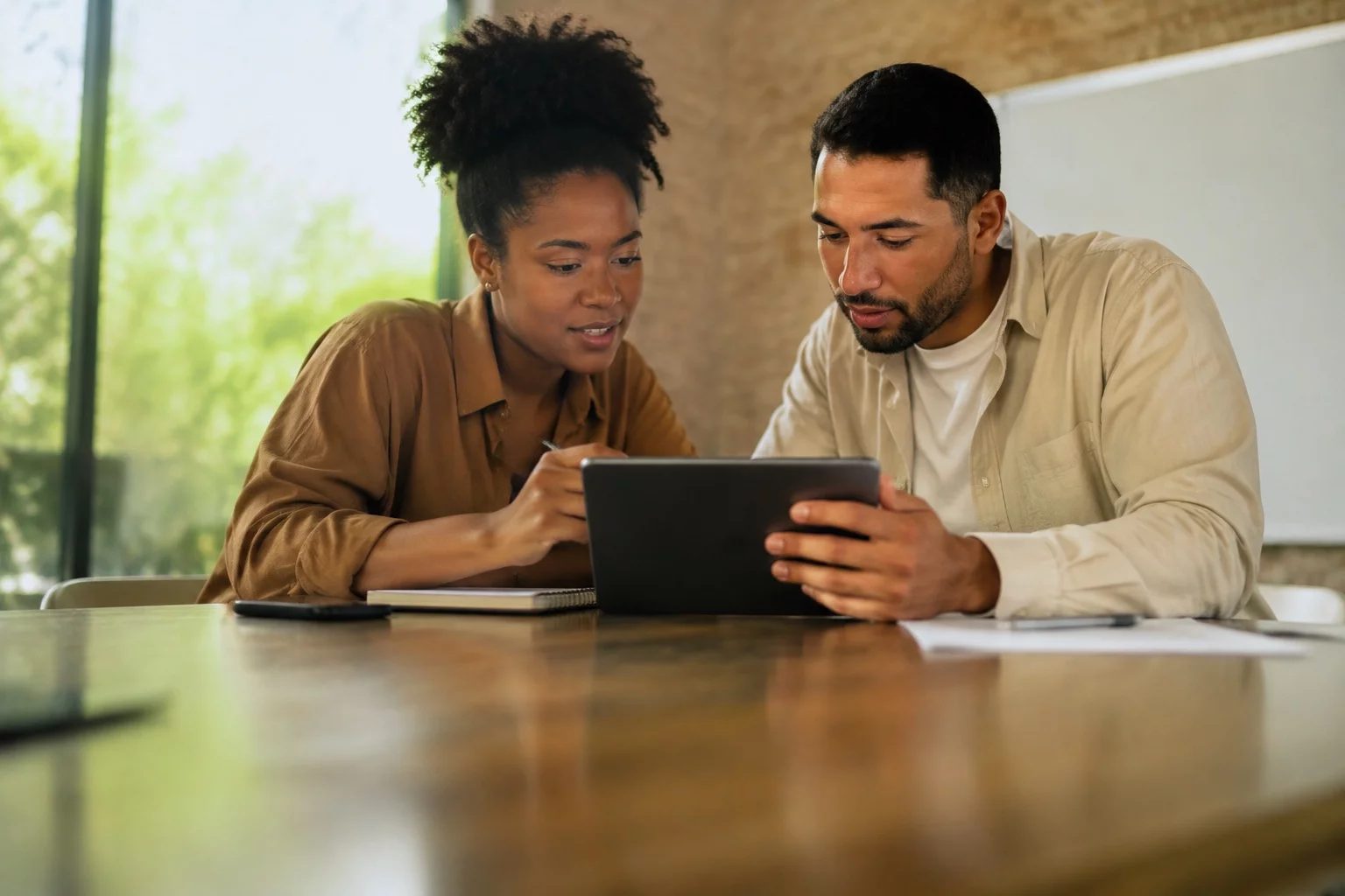 Duas pessoas revisando anotações em um tablet sobre uma mesa de madeira
